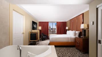 Habitación de hotel con una bañera grande, una cama con ropa blanca, un escritorio con una silla y vistas a un edificio a través de la ventana.