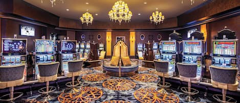 Um cassino com várias máquinas caça-níqueis, banquetas de bar e lustres.