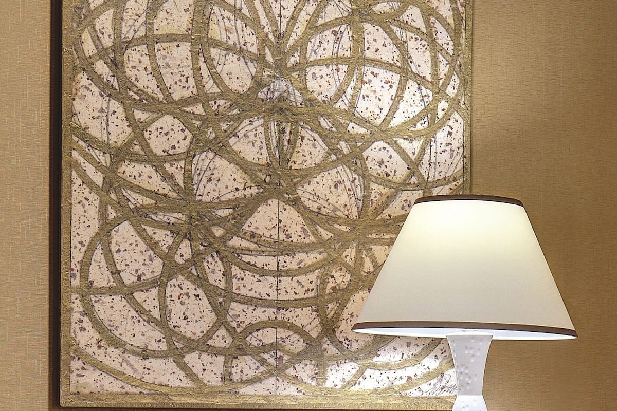 Een kamer met een houten bureau, een gestreept fauteuil, een witte lamp en een groot abstract schilderij aan de muur.