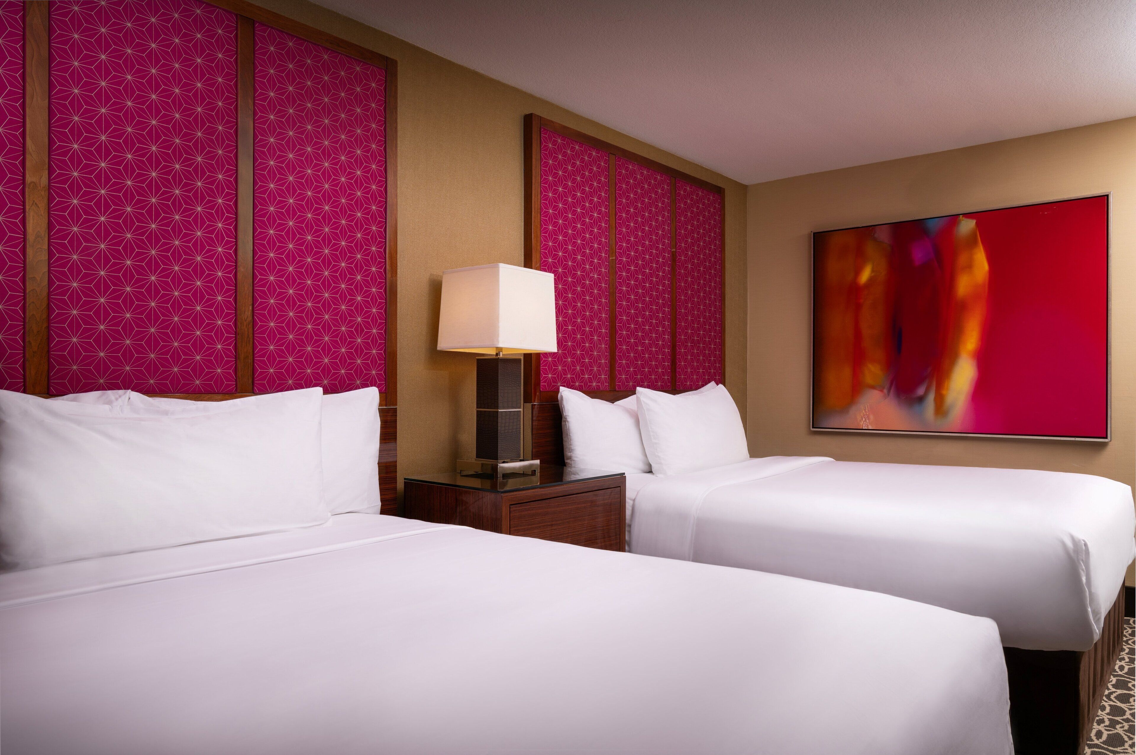 Une chambre d’hôtel avec deux lits, une table de chevet avec une lampe et un grand tableau abstrait accroché au mur.