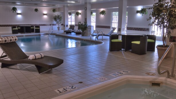 An indoor swimming pool area with lounge chairs, a hot tub, and potted plants. - Baymont by Wyndham Dallas/ Love Field (Dallas)