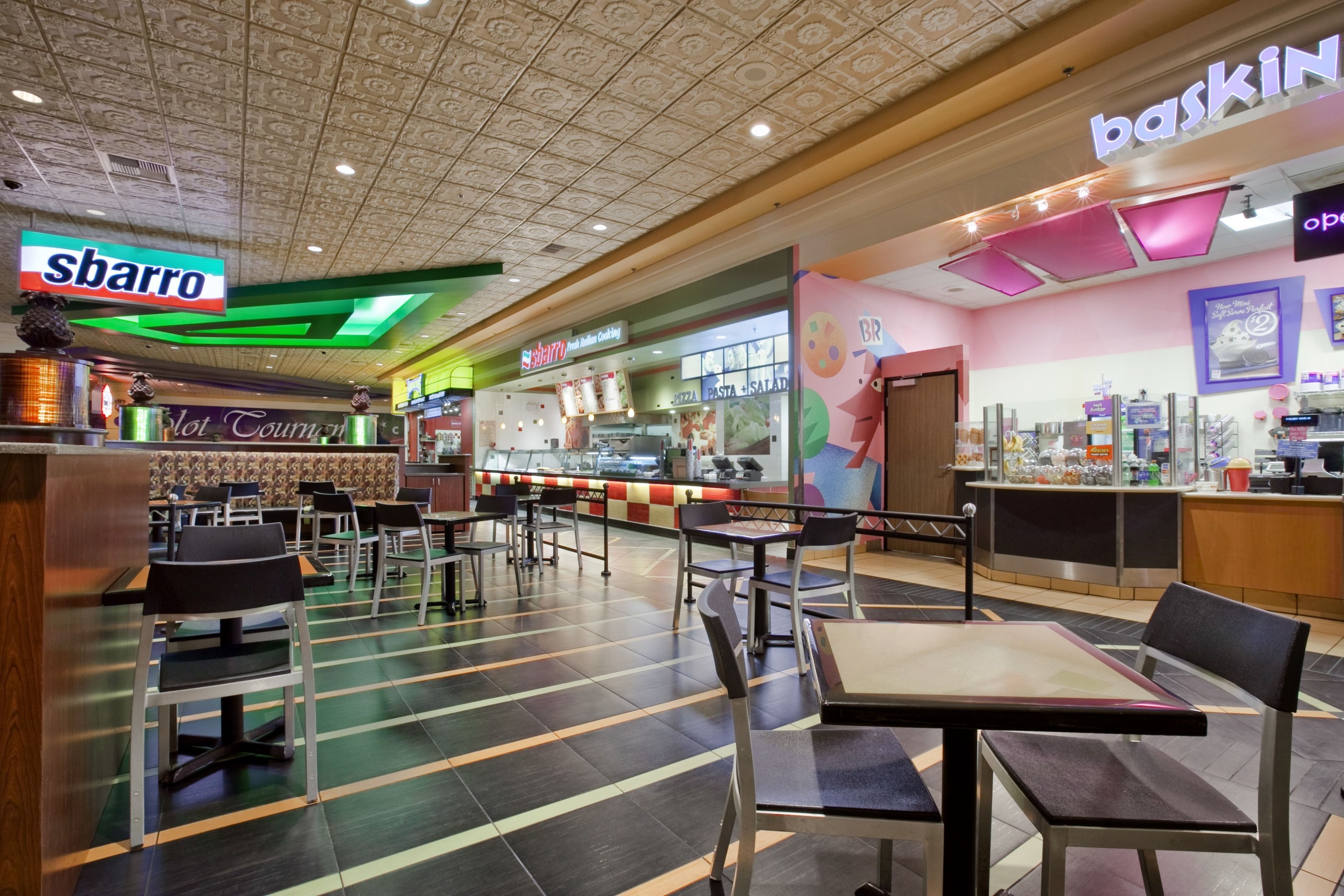 A restaurant with a modern interior, featuring a counter with a 'baskin' sign, a 'sbarro' sign, and a 'lot cooking' sign.