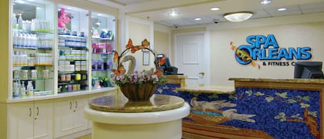 Un espace d’accueil comprenant un comptoir de réception, un présentoir de produits de toilette et un mur en mosaïque orné du nom du spa.