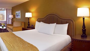 Une chambre d’hôtel avec un grand lit, un bureau avec une chaise, une télévision et une vue sur la ville par la fenêtre.