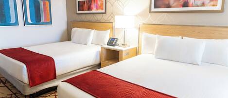 A hotel room with two beds, a nightstand with a lamp, and artwork on the walls.