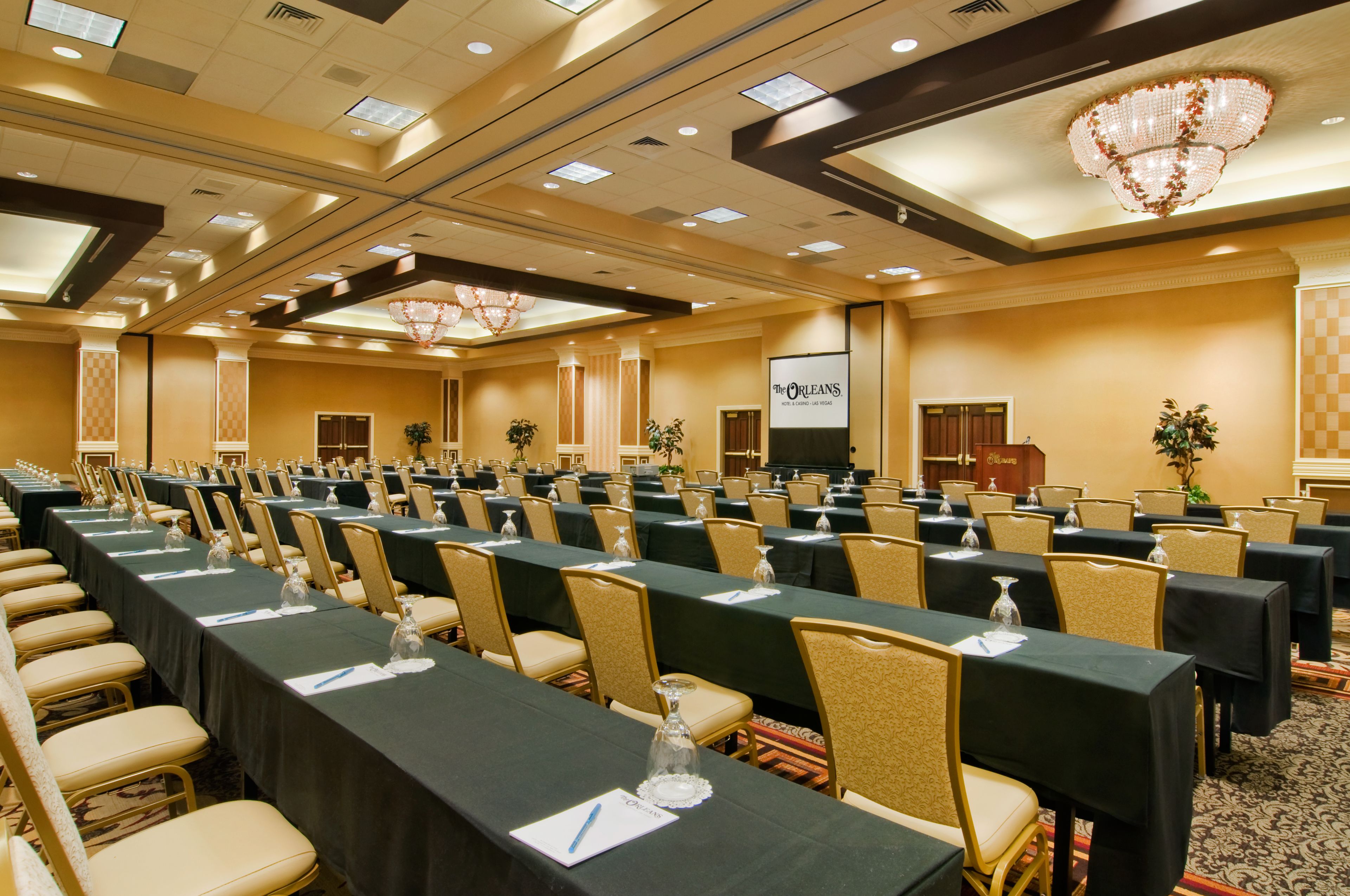 Une salle de conférence avec des rangées de tables, des chaises et un grand écran.