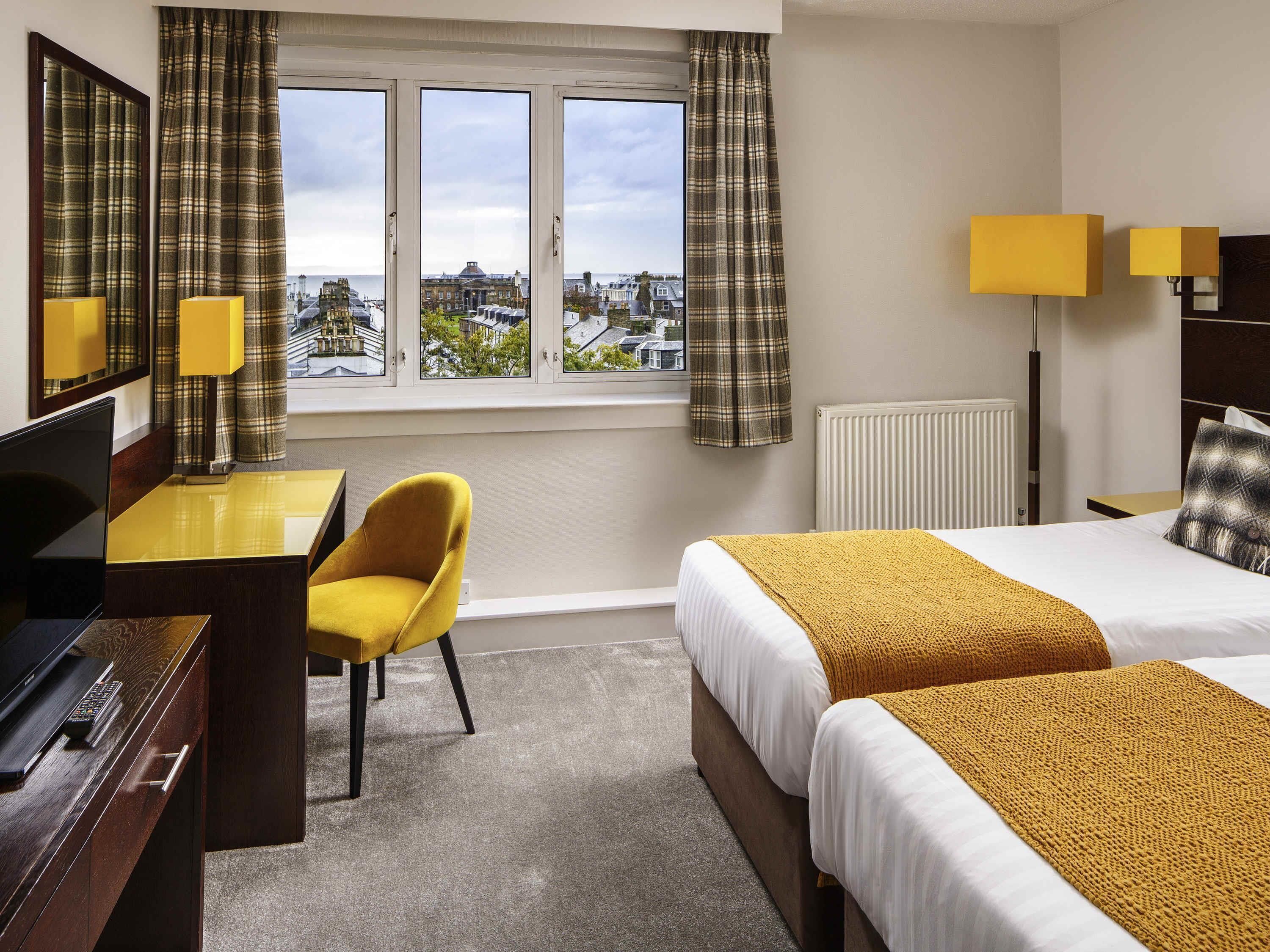 A hotel room with a bed, a desk, a chair, a TV, and a window with curtains.