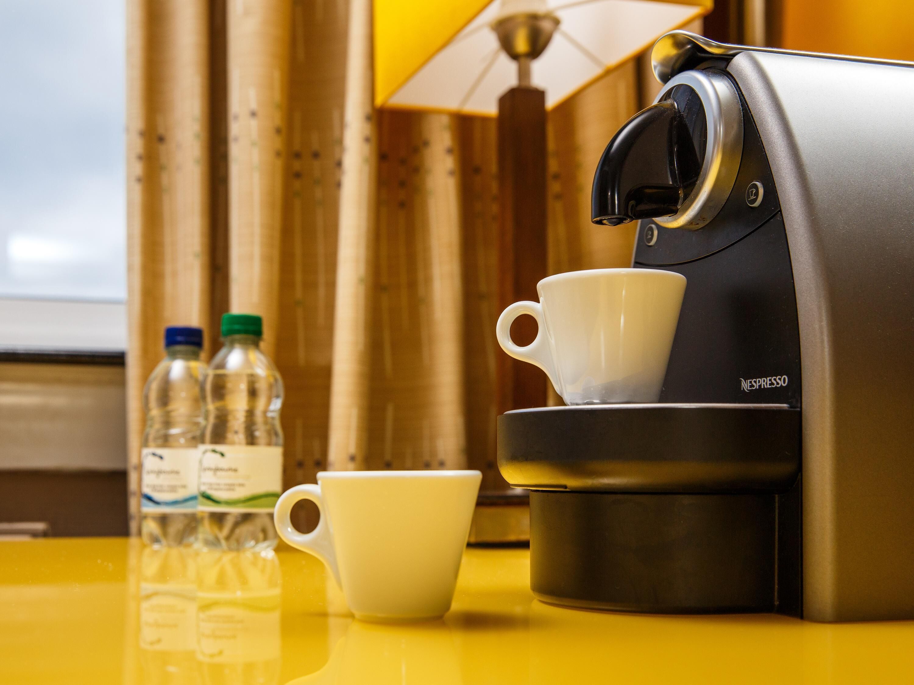 A Nespresso coffee machine with a cup and two water bottles on a yellow table.