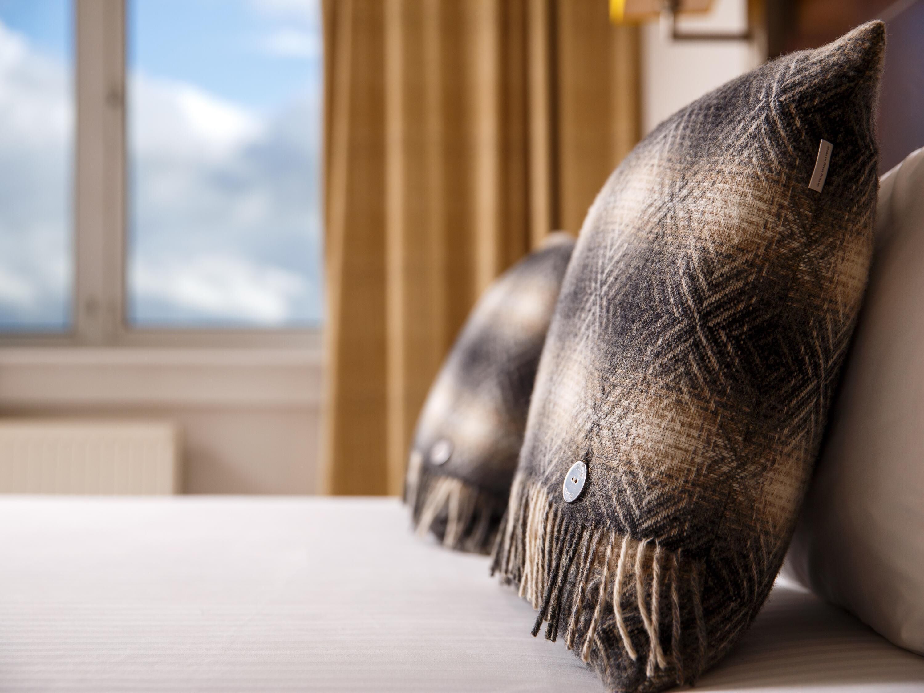 A bed with three textured pillows and a view of the sky through a window.