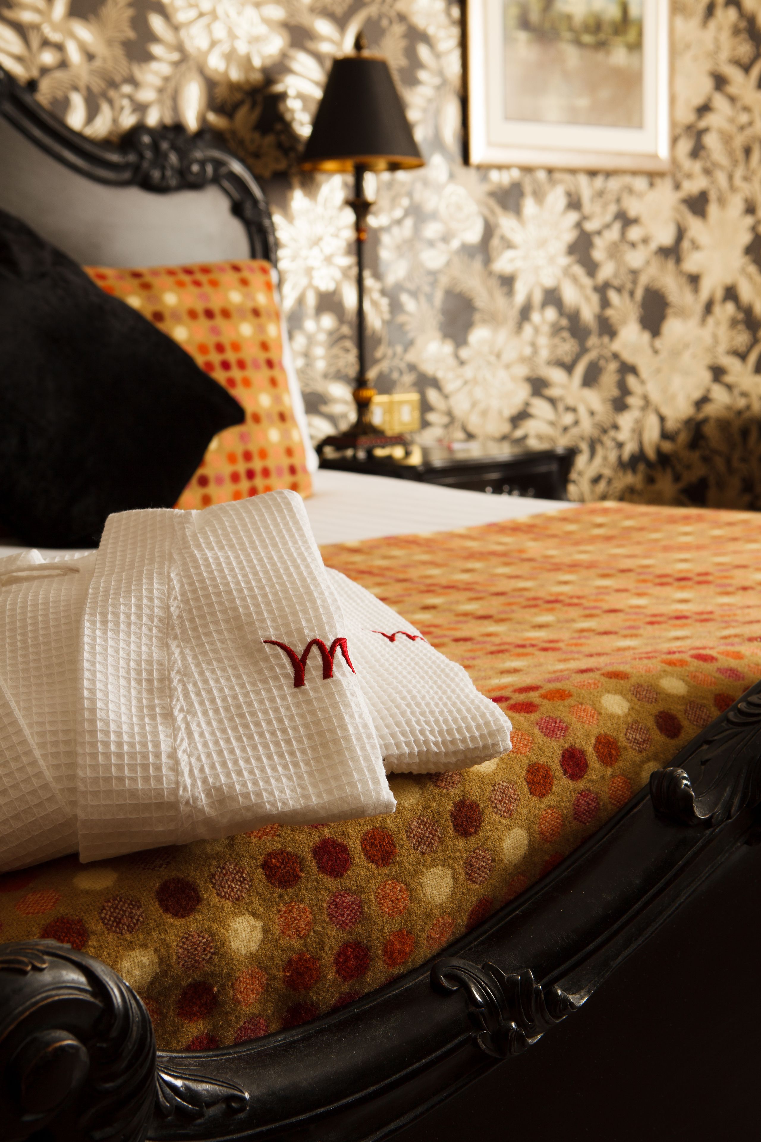 A neatly made bed with a patterned bedspread, a pillow with a monogram, and a black headboard.