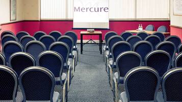 A conference room with rows of blue chairs, a projector screen with 'Mercure' on it, and a chandelier.