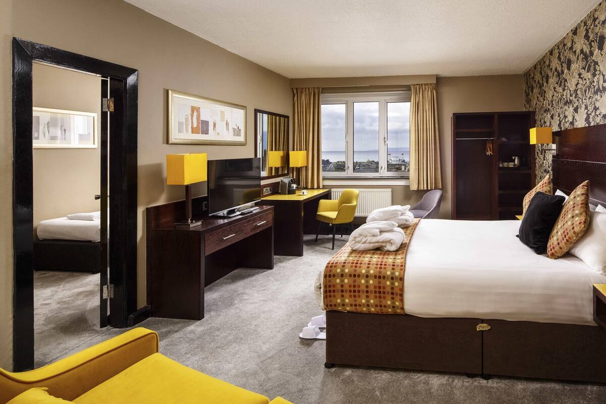 A hotel room with a bed, a desk, a chair, a TV, and a view of the city through the window.