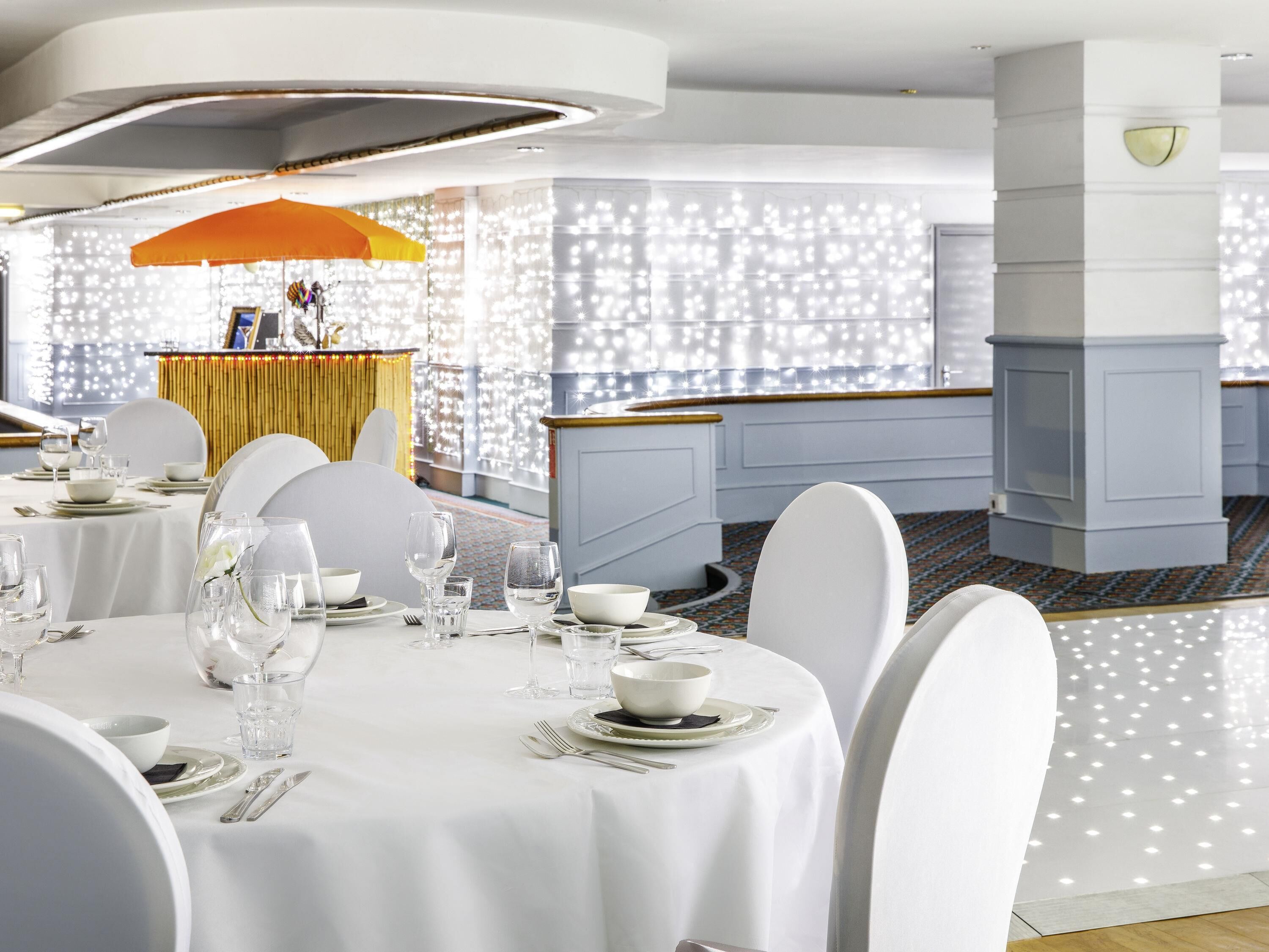 A dining area with round tables, white tablecloths, and chairs.