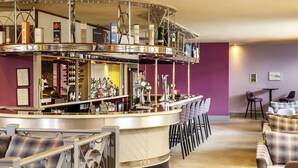 A bar area with a curved counter, multiple stools, and a variety of bottles and glasses. - Mercure Ayr Hotel (Ayr)