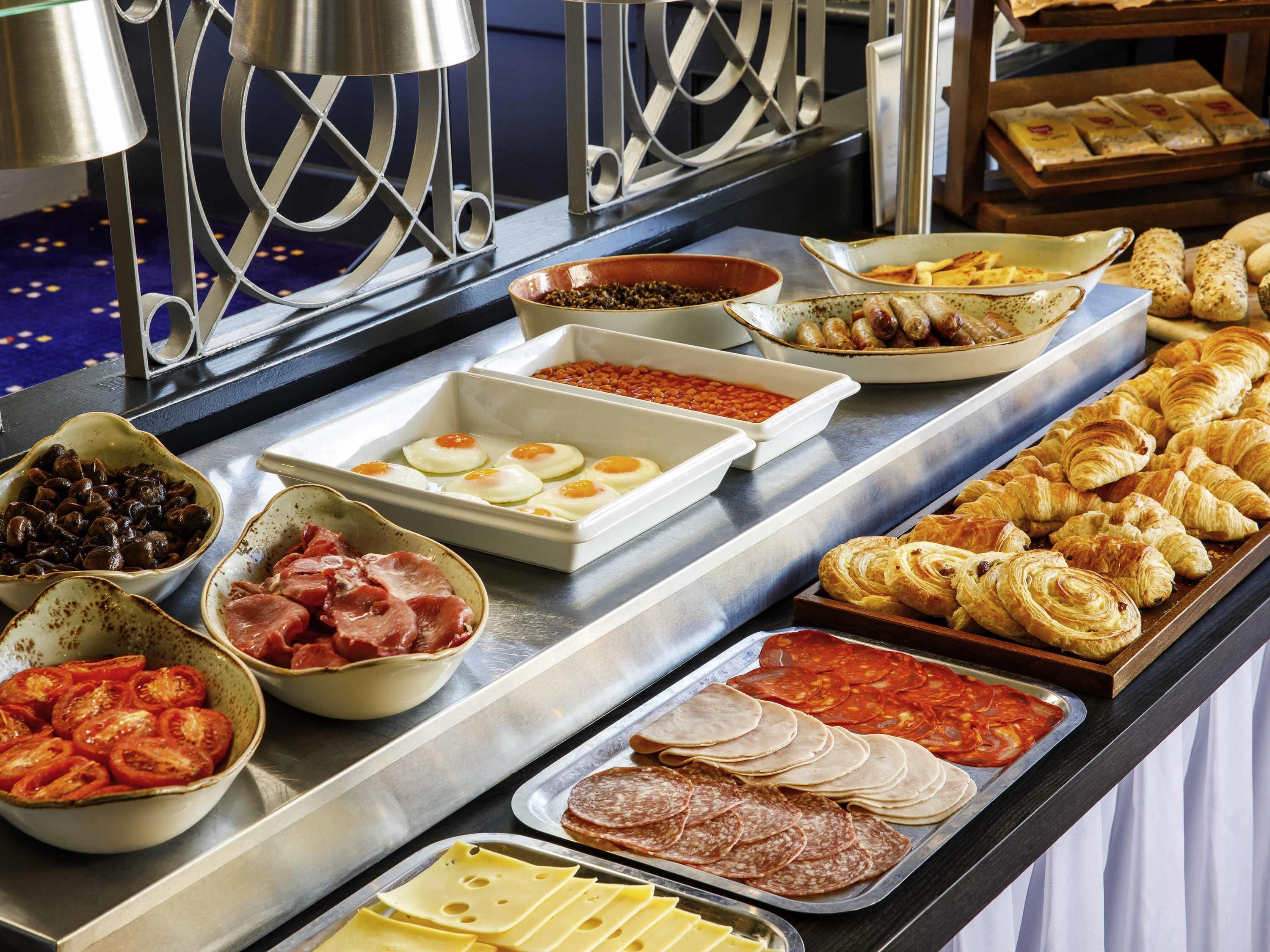 Un bufé con diversas opciones de comida, incluyendo huevos, carnes, quesos y pasteles.