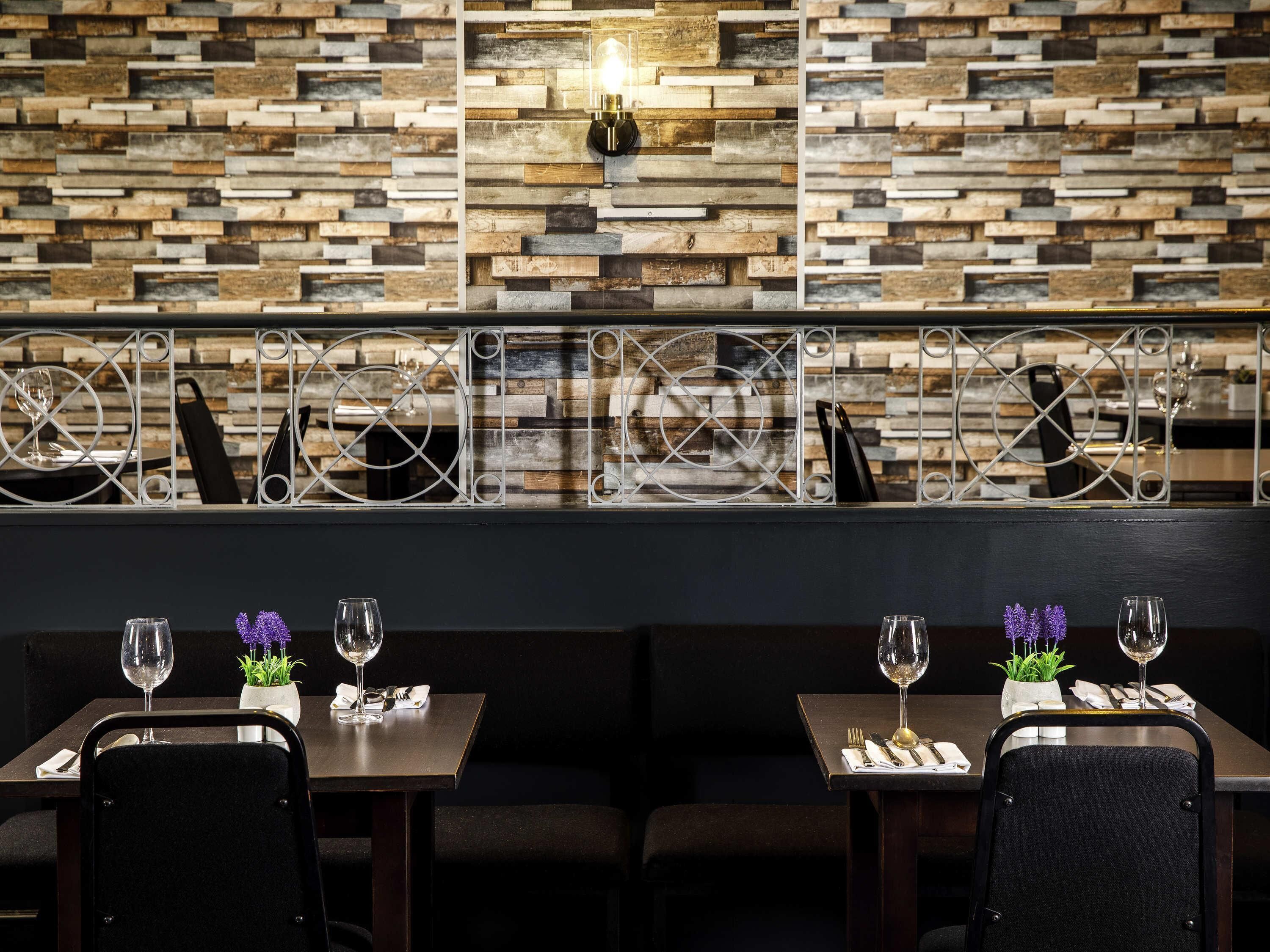 Een restaurantinterieur met een rustieke bakstenen muur, metalen leuningwerken en tafels gedekt met wijn glazen en bestek.