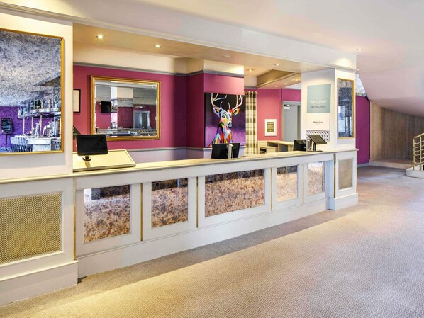 A reception area with a counter, a mirror, a colorful artwork, and a welcome sign. - Mercure Ayr Hotel (Ayr)