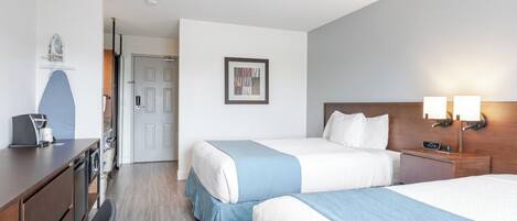 A hotel room with two beds, a desk with a coffee maker, a door, and a framed picture on the wall.
