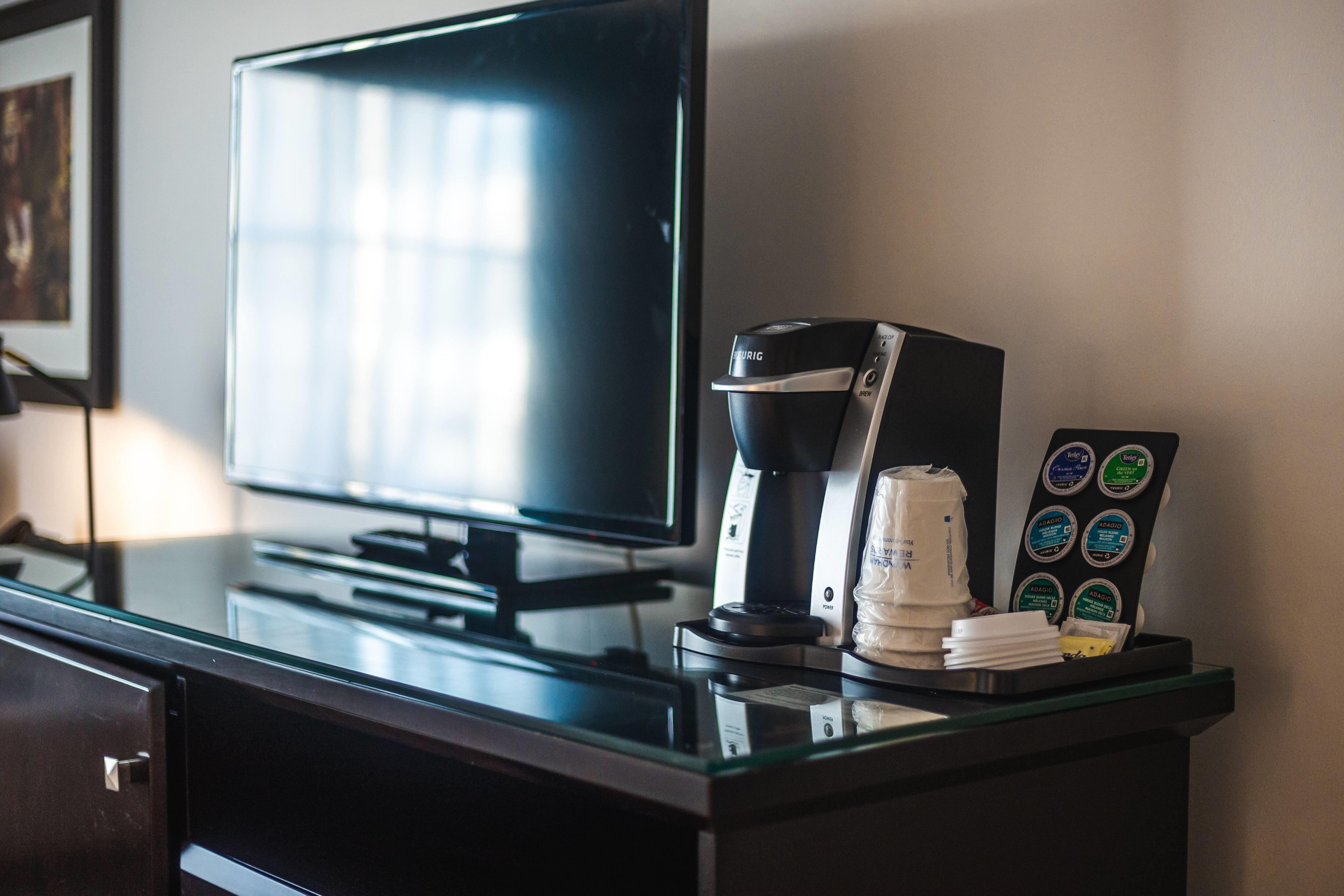 A hotel room with a flat-screen TV, a coffee maker, and a coffee pod holder on the counter.