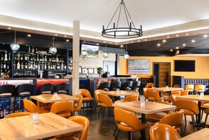 A restaurant interior with multiple tables and chairs, a bar area with bottles and glasses, and a large screen displaying a landscape. - Ramada by Wyndham Surrey/Langley (Surrey)
