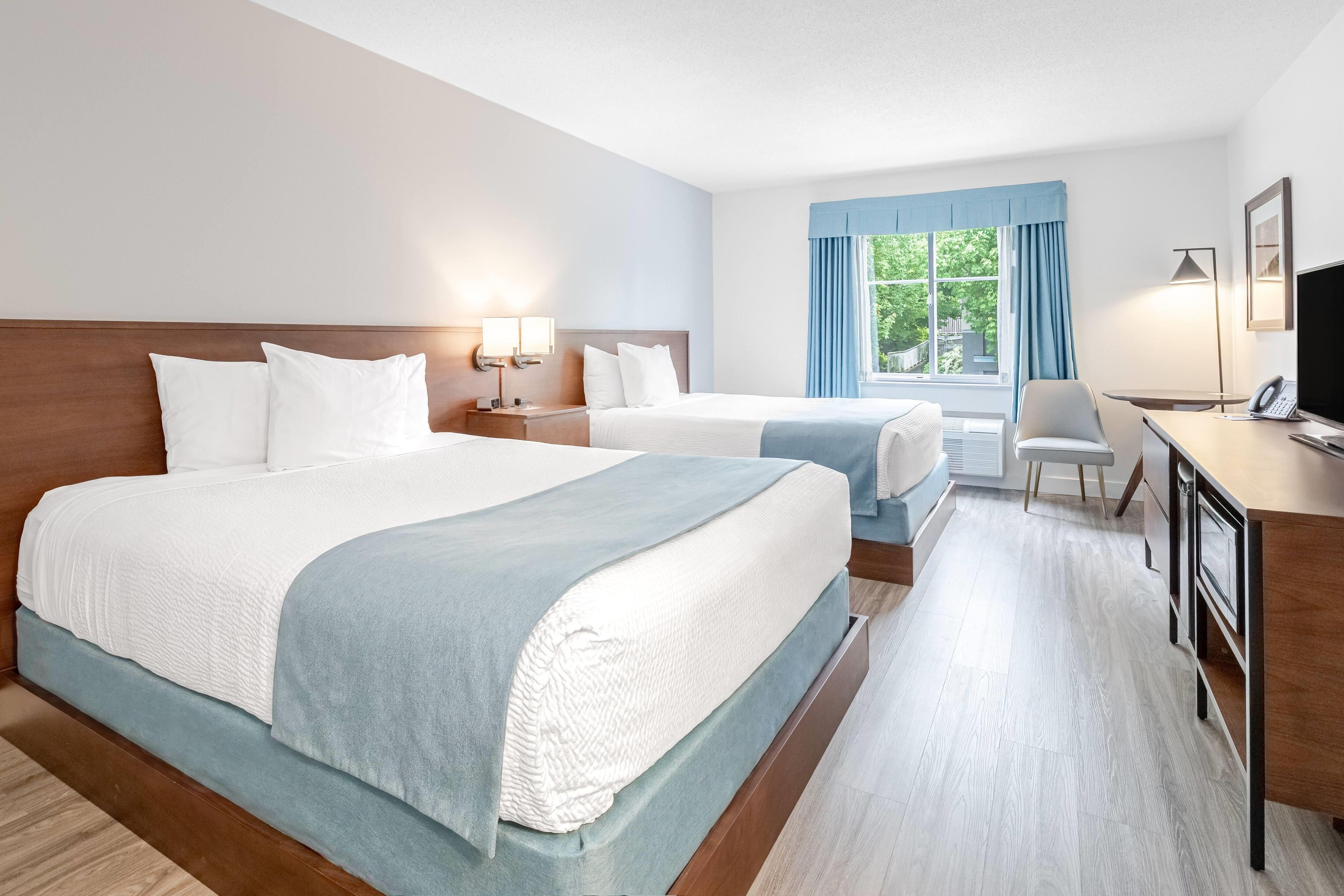A hotel room with two beds, a desk, a chair, and a window with curtains.