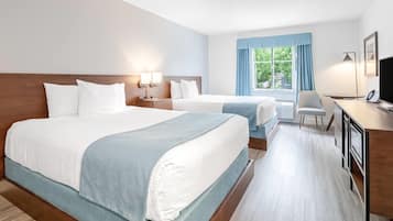 A hotel room with two beds, a desk, a chair, and a window with curtains.