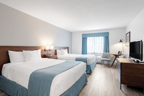 Habitación de hotel con dos camas, un escritorio, una computadora, un televisor y una ventana con cortinas.