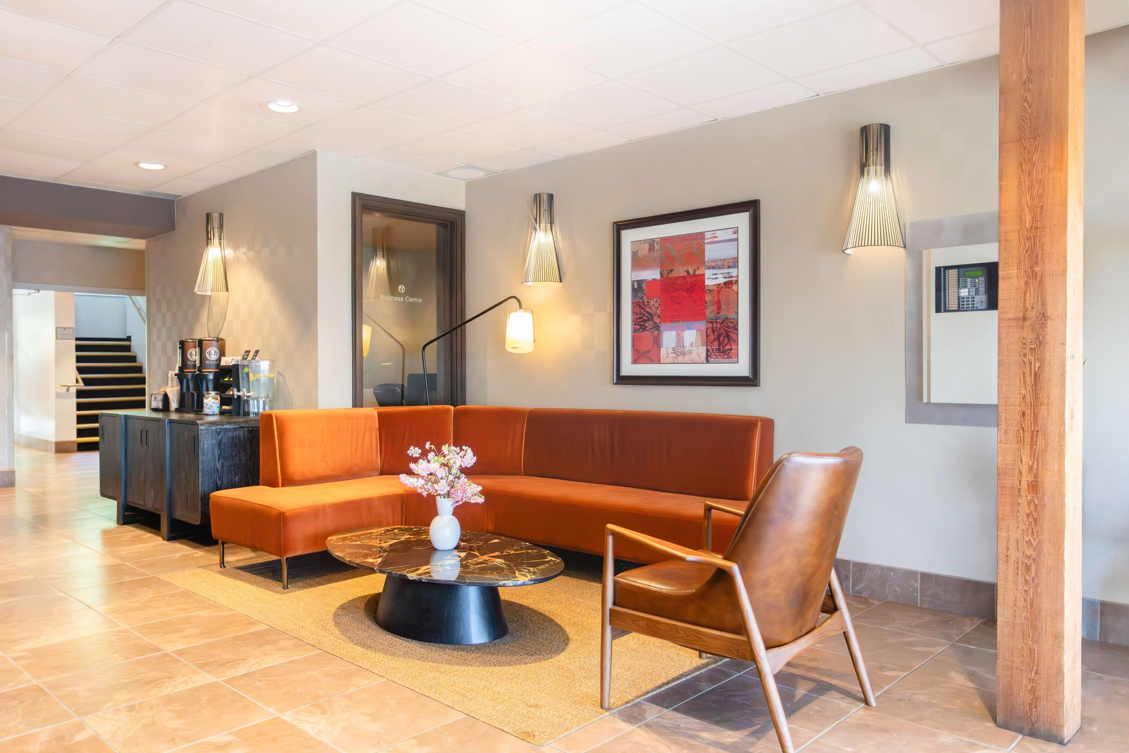 A modern lobby with a sectional sofa, a coffee station, and a framed abstract art piece.