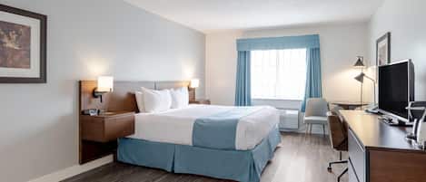 Habitación de hotel con cama, mesitas de noche, escritorio, silla, televisor y ventana con cortinas.