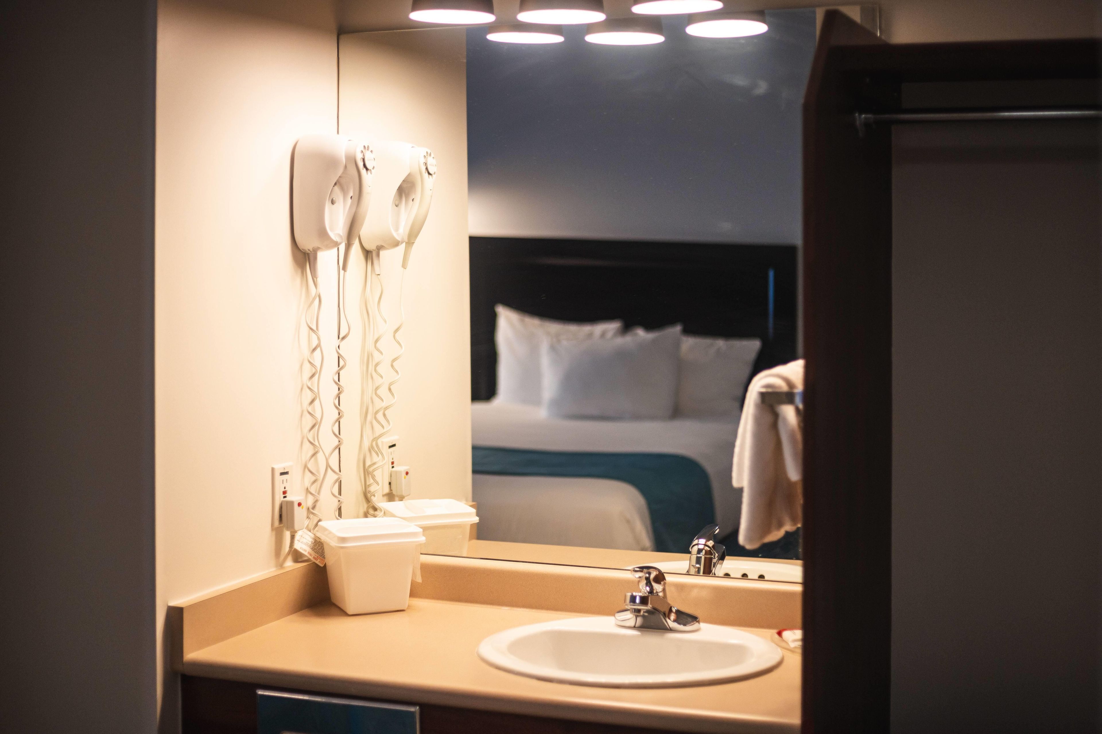 Un baño de hotel con un lavamanos, un espejo y secadores de pelo fijados en la pared.