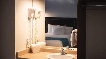 Un baño de hotel con un lavamanos, un espejo y secadores de pelo fijados en la pared.