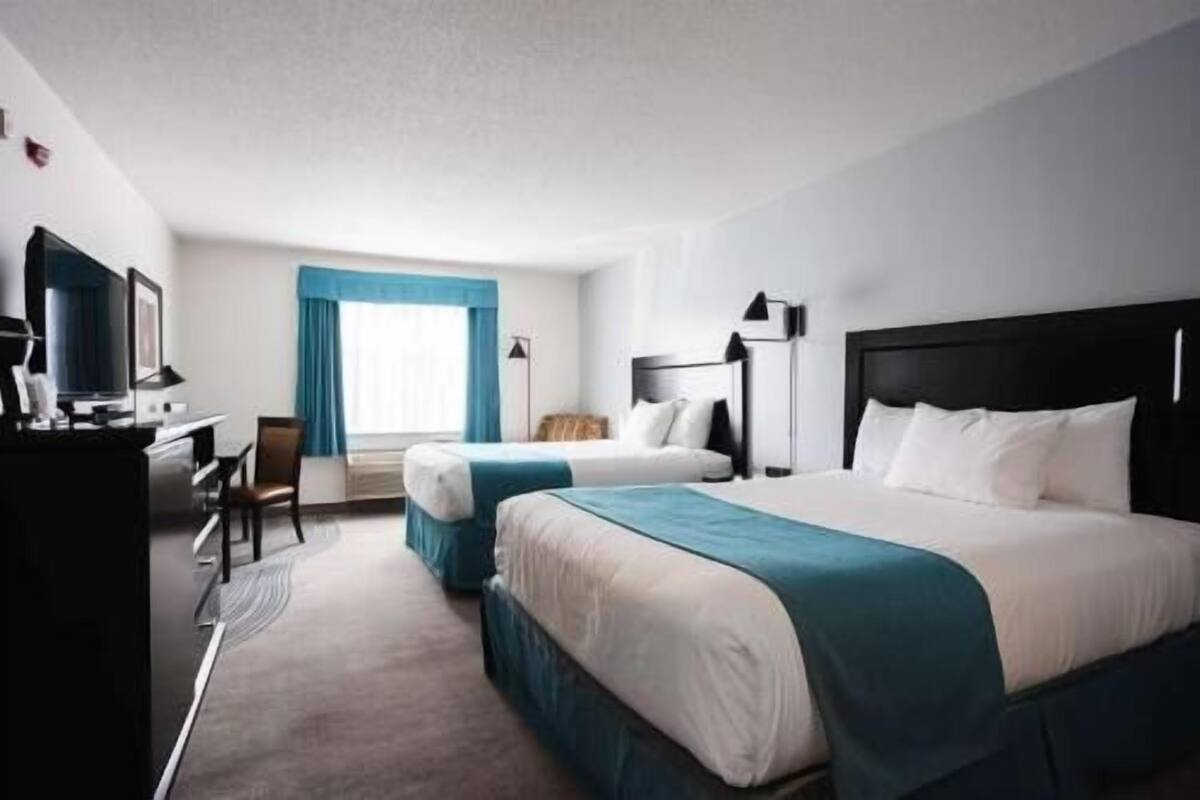 A hotel room with two beds, a desk, a chair, and a television.