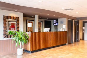A reception desk with a wooden panel design, a potted plant, and a flat-screen TV mounted on the wall. - Ramada by Wyndham Surrey/Langley (Surrey)