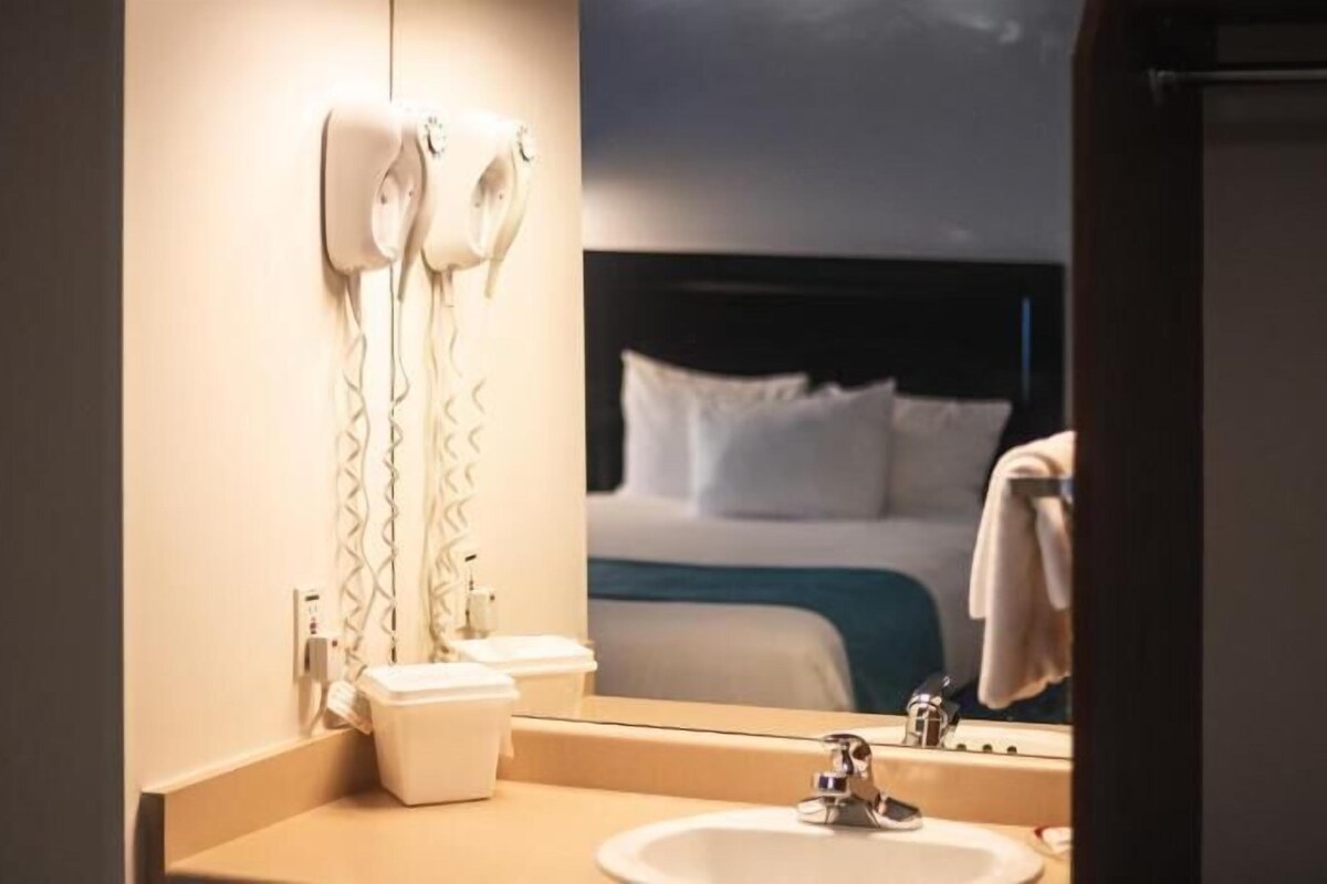 A hotel bathroom with a sink, mirror, and hair dryers.