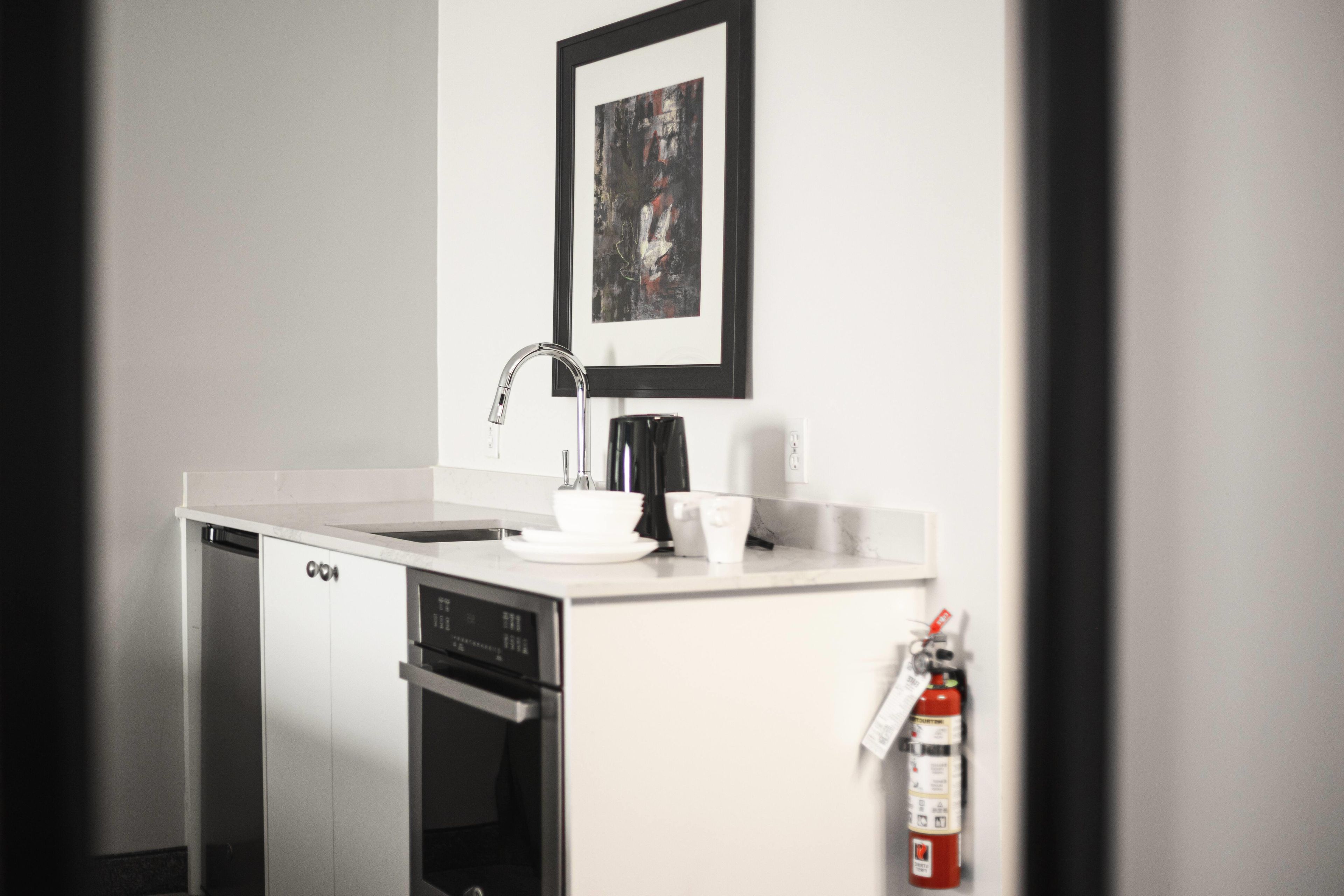 A compact kitchenette with a dishwasher, a coffee machine, and a fire extinguisher.
