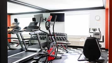Un gimnasio con cintas de correr, bicicletas estáticas y mancuernas.