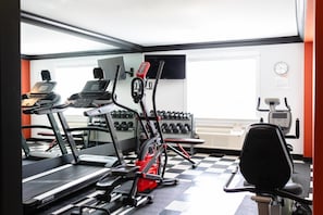 Un gimnasio con cintas de correr, bicicletas estáticas y mancuernas.