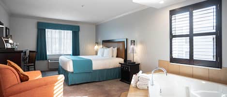 A hotel room with a bed, a desk, a chair, a large window, and a bathtub.