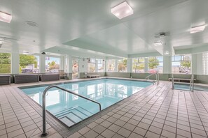 Una piscina con suelo de baldosas, una escalera metálica y un banco.