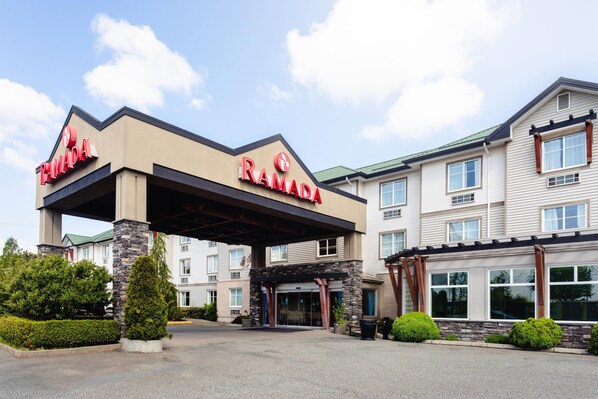 A building with a prominent 'RAMADA' sign, a covered entrance, and a parking area. - Ramada by Wyndham Surrey/Langley (Surrey)