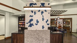 A reception area with a modern design, featuring a central counter with a marble top, a decorative wall with geometric patterns, and a wooden ceiling. - Hyatt Place Memphis Primacy Park (Memphis)