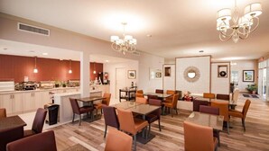 A spacious dining area with multiple tables and chairs, a kitchen area with wooden cabinets, and a decorative wall with a circular design. - Best Western Mountainview Inn (Golden)