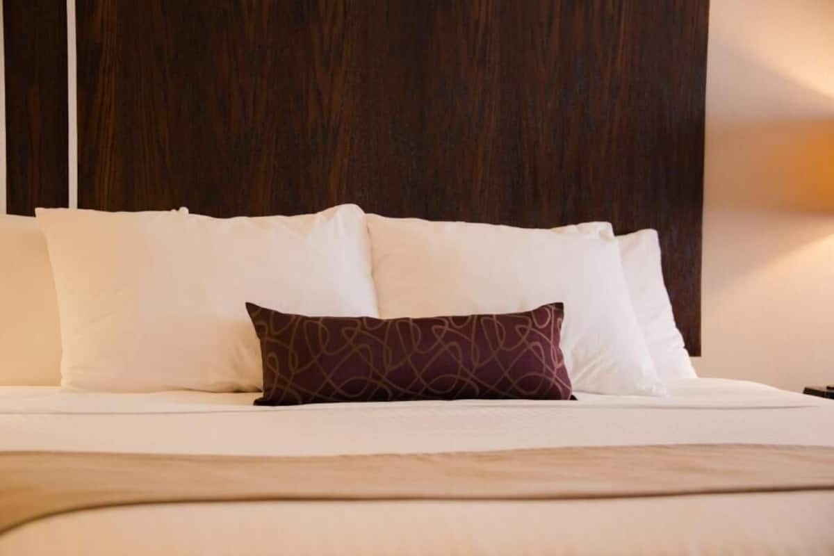 Una cama bien hecha con ropa de cama blanca y una sola almohada estampada.