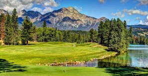 Ein Golfplatz mit Teich, umgeben von Bäumen und Bergen.