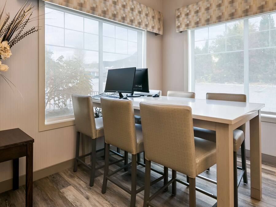 A modern office space with a large window, a desk with a computer, and four chairs.