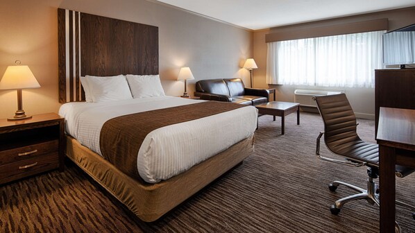 A hotel room with a large bed, a desk, a chair, a lamp, and a TV.