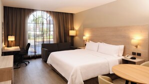 Een hotelkamer met een groot bed, een bureau, een stoel, een klein tafeltje en een raam met gordijnen.