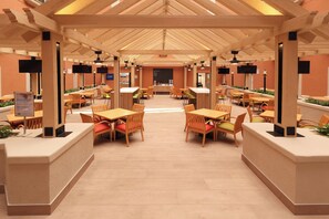Un comedor interior amplio con mesas y sillas de madera, una barra central y un techo alto con vigas de madera.