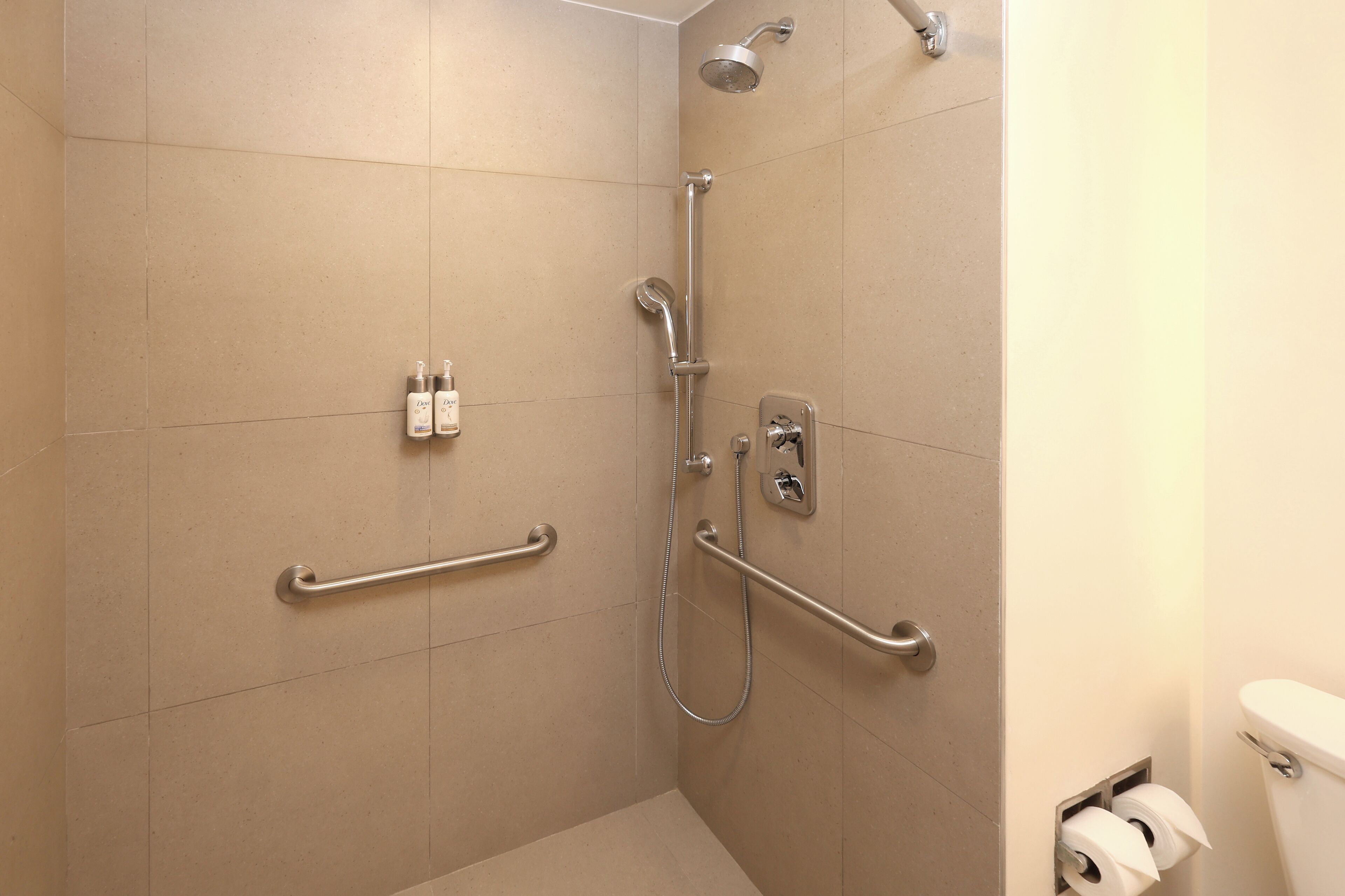 Un baño con baldosas color beige, y una ducha con cabezal de ducha manual.