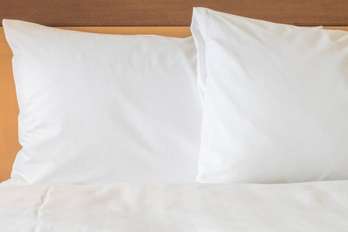 Una cama con ropa blanca y almohadas frente a un cabecero de madera.